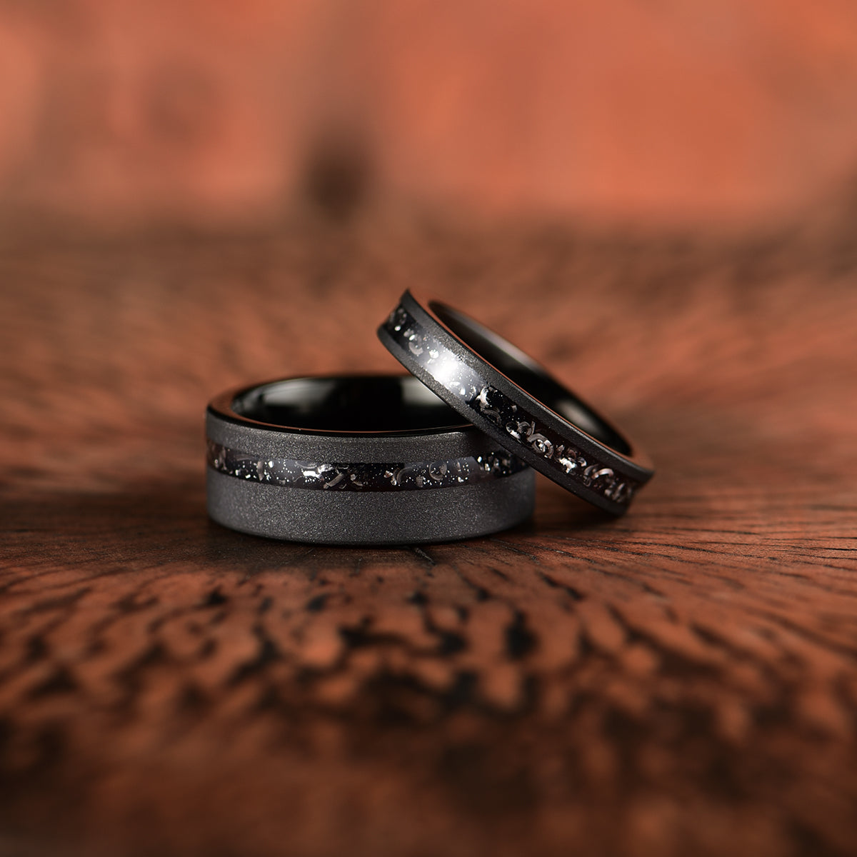 Two crushed meteorite inlay sandblasted black tungsten men's wedding band laid down on top of eachother